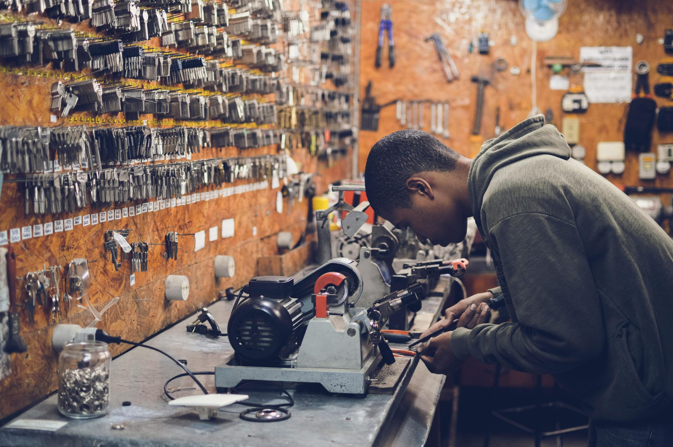 A focused craftsman works in a key-making workshop surrounded by tools and equipment.