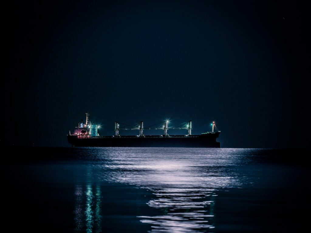 A tranquil nighttime scene of a cargo ship floating on a calm ocean under a starlit sky.