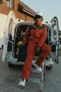 Portrait of an adult worker in red coveralls sitting by a van outdoors.